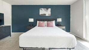 Een slaapkamer met een bed, twee nachtkastjes met lampen, een dressoir en een wanddecoratie.