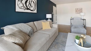 Un salon moderne avec un canapé beige, une petite table agrémentée d’objets décoratifs, un fauteuil gris et un mur d’accent bleu foncé.