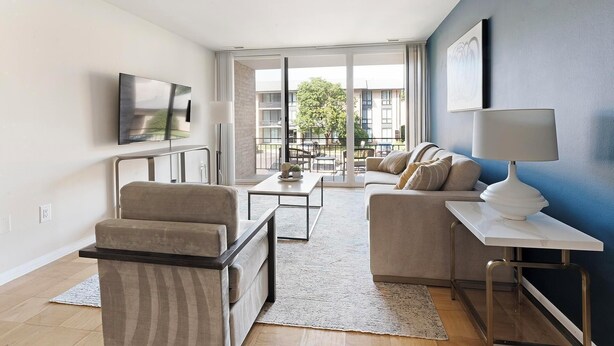 Un salon moderne comprenant un canapé, un fauteuil, une table basse et un téléviseur fixé au mur.