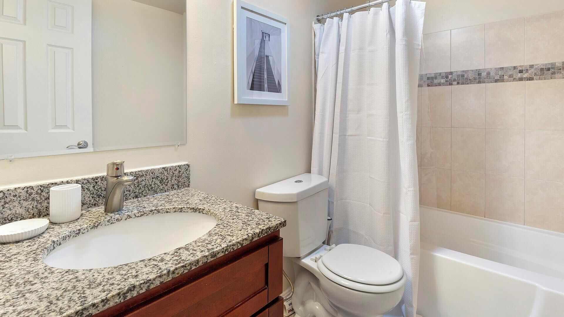 A bathroom with a granite countertop sink, a toilet, and a bathtub.