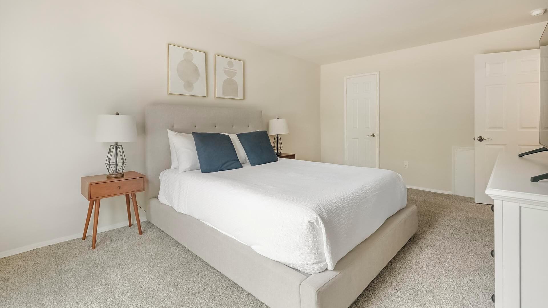 Une chambre à coucher comprenant un lit, deux tables de chevet, une commode, une coiffeuse et deux tableaux encadrés accrochés au mur.