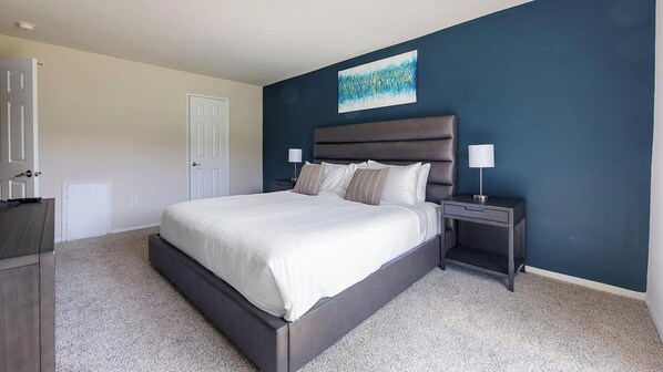A bedroom with a large bed, a nightstand, a dresser, and a door.