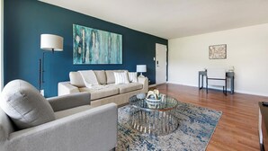 Un salon moderne avec un canapé beige, une table basse en verre et un tableau abstrait bleu accroché au mur.