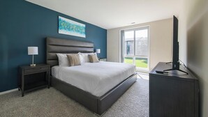Une chambre moderne avec un grand lit, une table de chevet, un téléviseur posé sur un meuble et une fenêtre donnant sur l’extérieur.