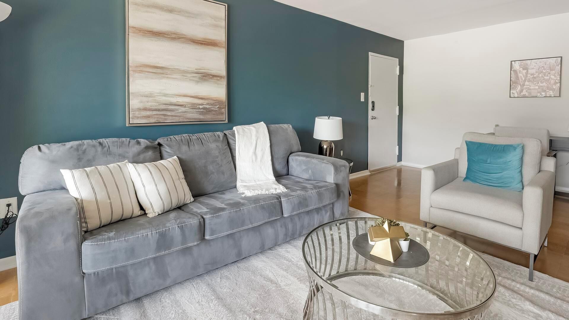A modern living room with a grey sofa, a white armchair, and a glass coffee table.