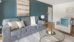 Un salon moderne avec un canapé gris, un fauteuil blanc et une table basse en verre.