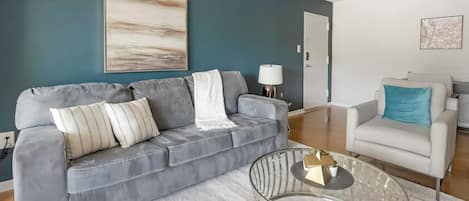 A modern living room with a grey sofa, a white armchair, and a glass coffee table.