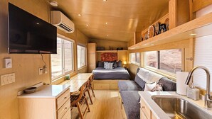 A compact, well-lit room with a bed, a small kitchenette, a seating area, and a large window offering a view. - Cozy Tiny Home @ Private Moab Ranch (Moab)