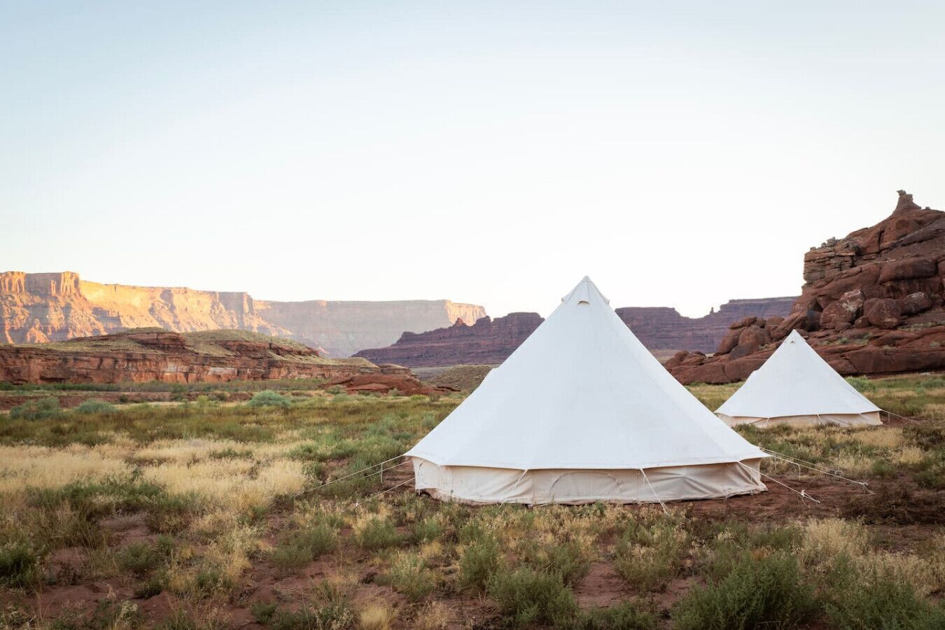 Two white tents set up in a natural landscape with rocky cliffs in the background.