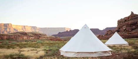 Two white tents set up in a natural landscape with rocky cliffs in the background.