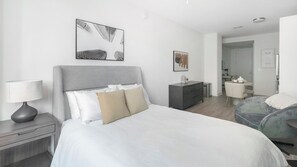 A modern hotel room with a large bed, a bedside table with a lamp, a dresser, and a chair. - Landing | Beautiful Studio, Rooftop Lounge, Gym (Birmingham)