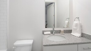 A modern bathroom with a white toilet, granite countertop sink, and a large mirror. - Landing | Beautiful Studio, Rooftop Lounge, Gym (Birmingham)