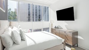 Ett modernt sovrum med en stor säng, ett nattduksbord, en byrå och en tv som är monterad på väggen.