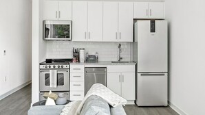 Cocina compacta con armarios blancos, microondas integrado, estufa, lavavajillas y refrigerador.