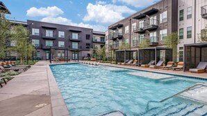 A swimming pool area with lounge chairs and a building with balconies.