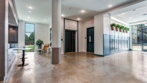 A modern lobby with a seating area, a large pillar, and a row of lockers. - Landing | Spectacular Studio, Courtyard, Gym (Denton)