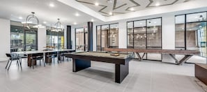 A modern indoor recreational area with a pool table, dining table, chairs, and large windows.