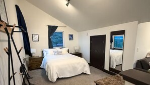 A bedroom with a bed, a desk, a chair, a wardrobe, and a window with a view.