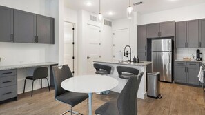 A modern kitchen with grey cabinets, a stainless steel refrigerator, a round dining table with grey chairs, and a small island with a sink and bar stools.