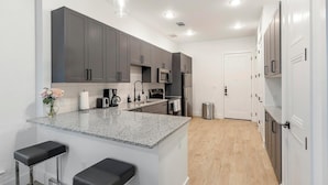 A modern kitchen with granite countertops, stainless steel appliances, and grey cabinetry. - Landing | Modern 1BD, Pool, Gym (Denton)