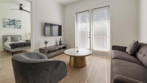 A modern living room with a sofa, a chair, a coffee table, a TV, and a ceiling fan. - Landing | Incredible 1BD, Clubhouse, Gym (Denton)