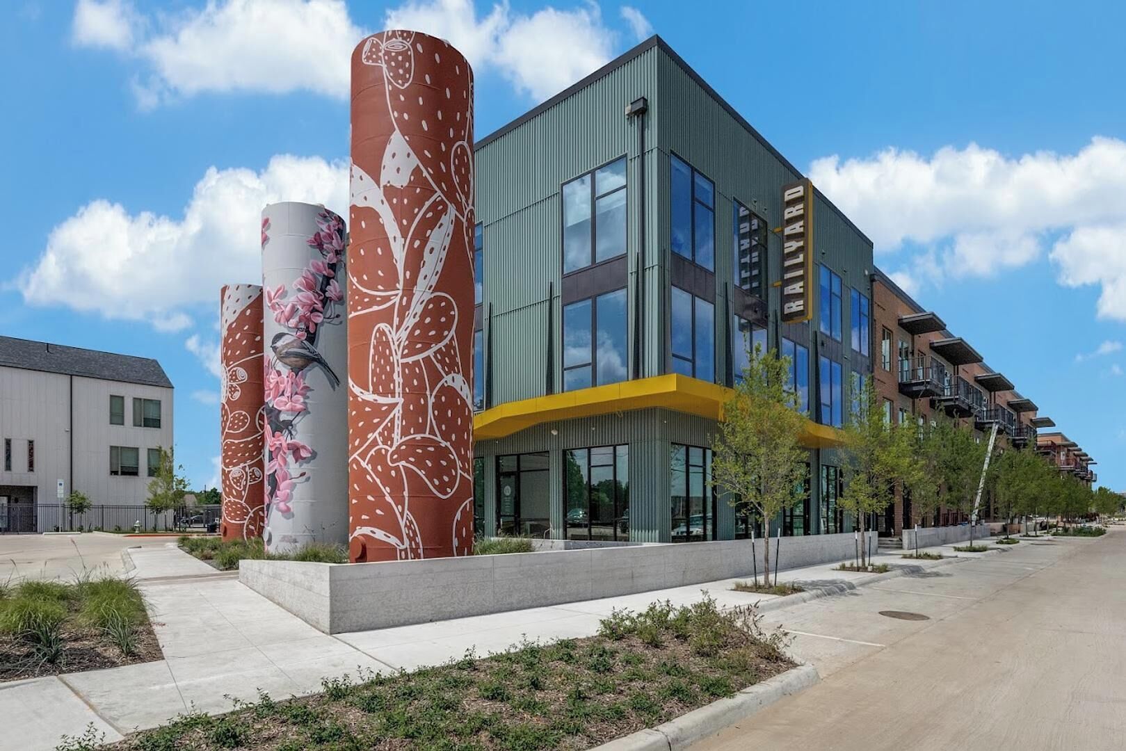 A modern building with large cylindrical columns, a flat roof, and a mix of glass and brick facades.