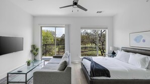 A modern bedroom with a bed, a sofa, a TV, and a balcony with a view of trees. - Landing | Stunning Studio, Pool, Clubhouse (Denton)