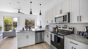 A modern kitchen with white cabinets, stainless steel appliances, and a large window offering a view of the outdoors. - Landing | Stunning Studio, Pool, Clubhouse (Denton)