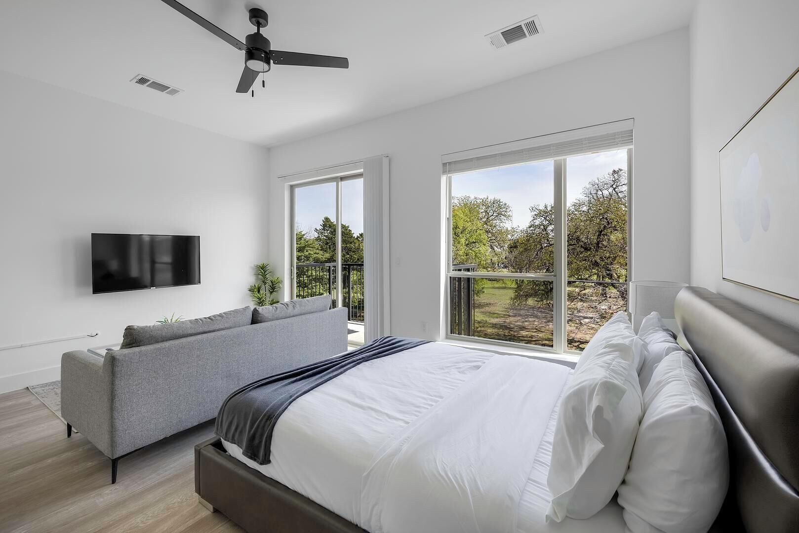 Une chambre moderne avec un grand lit, un canapé gris, un ventilateur de plafond et un téléviseur.