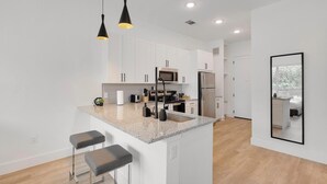 A modern kitchen with white cabinets, a granite countertop, stainless steel appliances, and two bar stools.