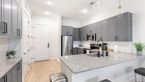 A modern kitchen with grey cabinets, stainless steel appliances, granite countertops, and a central island. - Landing | Beautiful 1BD, Gym, Pool (Denton)