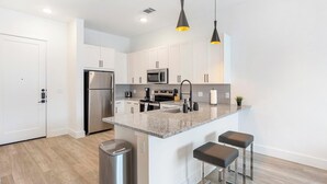 A modern kitchen with white cabinets, stainless steel appliances, a granite countertop, and two bar stools.