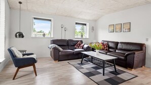A modern living room with two leather sofas, a coffee table, and a blue armchair. There are three windows providing natural light, and a ceiling with exposed beams. - Beautiful home in Tarm with WiFi (Tarm)