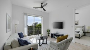 Un salon moderne avec un canapé, un fauteuil, une table basse et un téléviseur fixé au mur.