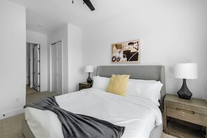 Une chambre d’hôtel moderne avec un grand lit, deux tables de chevet avec des lampes, une tête de lit et une œuvre d’art accrochée au mur.