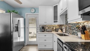 A modern kitchen with stainless steel appliances, white cabinetry, a tiled backsplash, and a window with blinds.
