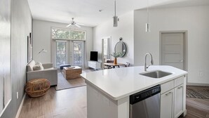 A modern kitchen with a central island, a built-in dishwasher, and a dining area with a round table and chairs. - Landing | Chic 1BD, Gym, Rooftop Lounge (San Antonio)