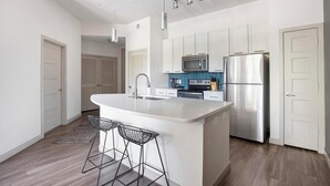 A modern kitchen with a central island, stainless steel appliances, and a minimalist design. - Landing | Chic 1BD, Gym, Rooftop Lounge (San Antonio)