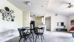 Ein modernes Wohnzimmer mit Essbereich, einer Küche im Hintergrund und einem an der Wand montierten Fernseher.