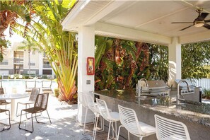 Zona de bar al aire libre con piscina, rodeada de sillas y exuberantes plantas tropicales.