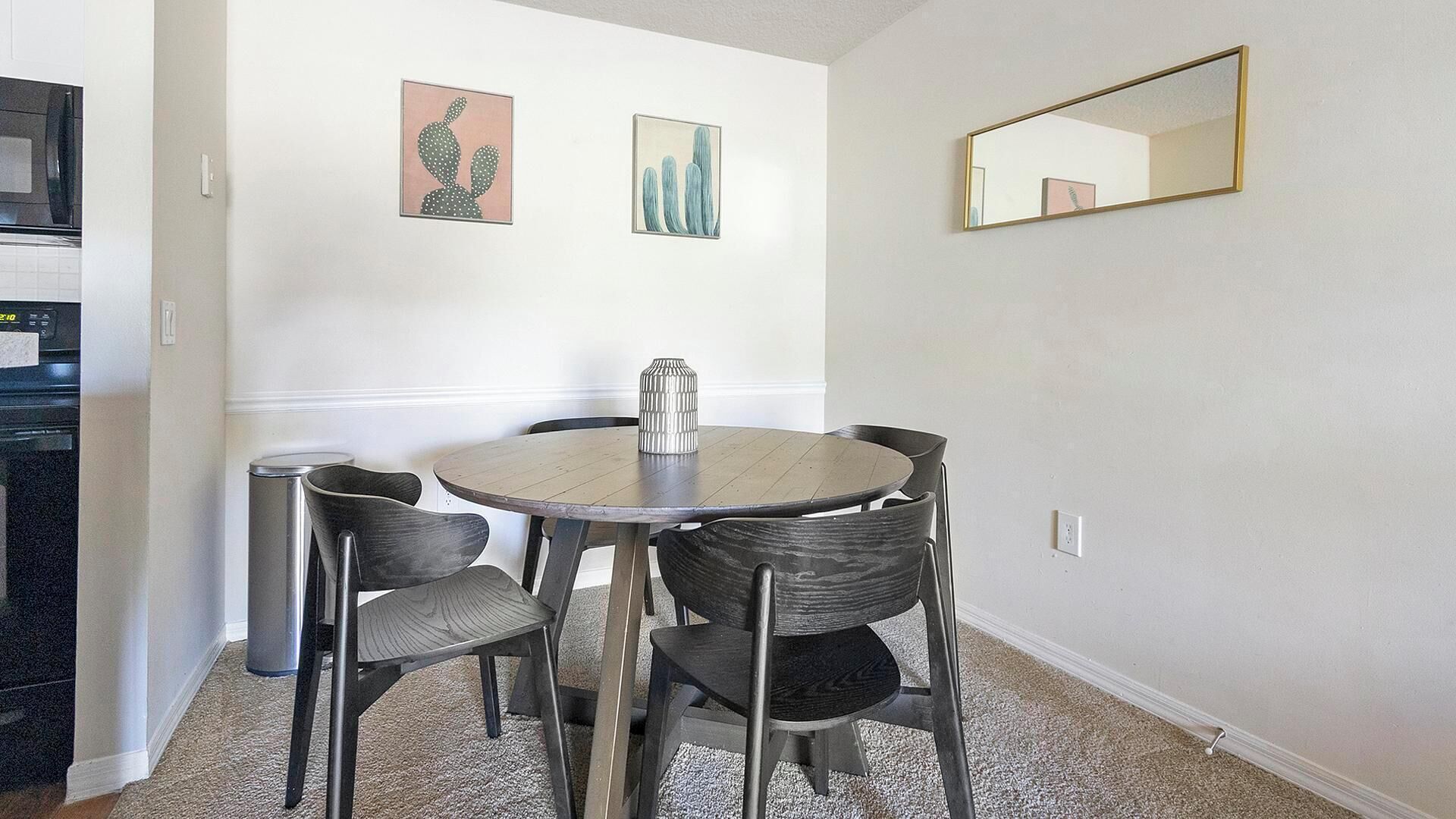 Un comedor con una mesa redonda, cuatro sillas, un jarrón y dos cuadros en la pared.