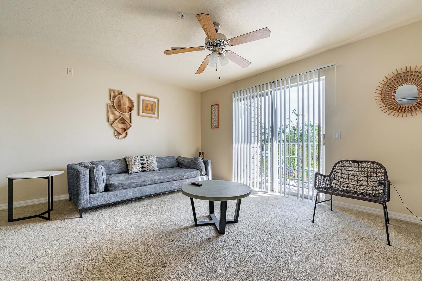 A living room with a gray sofa, a round coffee table, a wicker chair, and a ceiling fan.