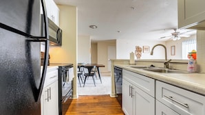 A kitchen with white cabinets, a black refrigerator, a wooden dining table, and a ceiling fan. - Landing | Incredible 2BD, Game Room, Gym (Longboat Key)