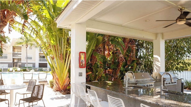 An outdoor bar area with a pool, surrounded by chairs and large tropical plants. - Landing | Incredible 2BD, Game Room, Gym (Longboat Key)