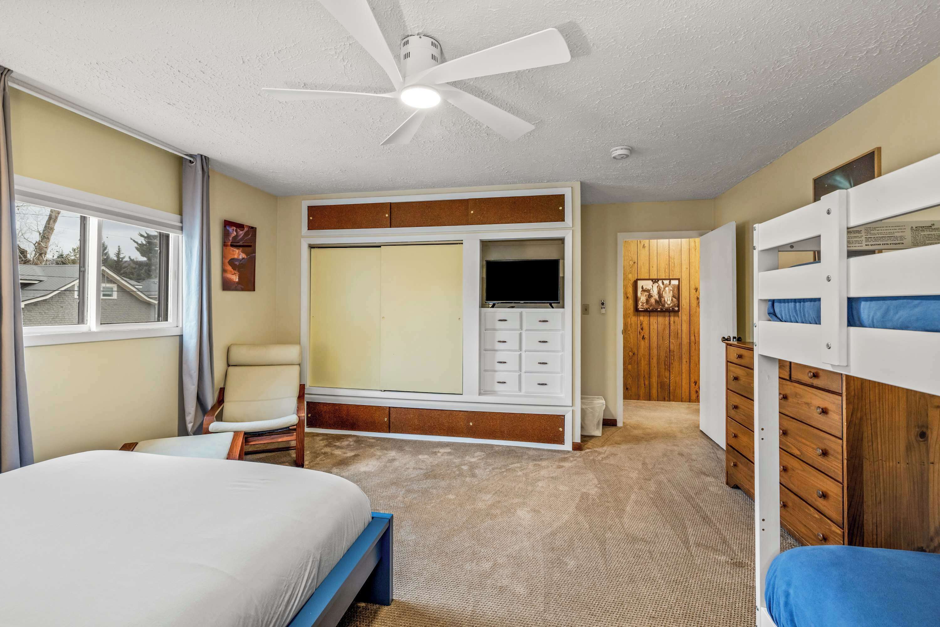 A bedroom with a bed, a chair, a wardrobe, a TV, and a bunk bed.