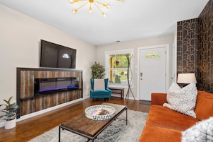 A living room with a flat-screen TV mounted on a wooden wall, a blue armchair, an orange sofa, and a coffee table with a decorative tray.