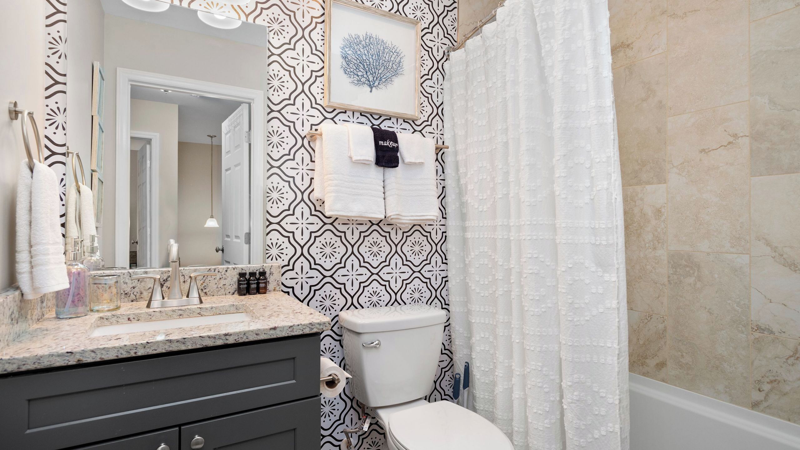 A bathroom with a patterned wall, a toilet, a sink with a mirror, and a towel rack.
