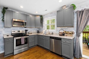 A modern kitchen with grey cabinets, stainless steel appliances, and a window with a view.