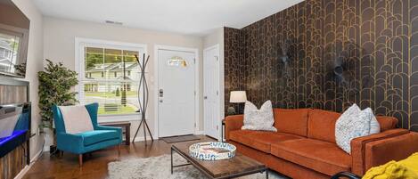 A modern living room with a blue armchair, orange sofa, and a wooden coffee table.