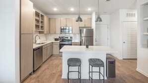 Una cocina moderna con armarios de madera, electrodomésticos de acero inoxidable, una isla central con taburetes de bar e iluminación colgante.